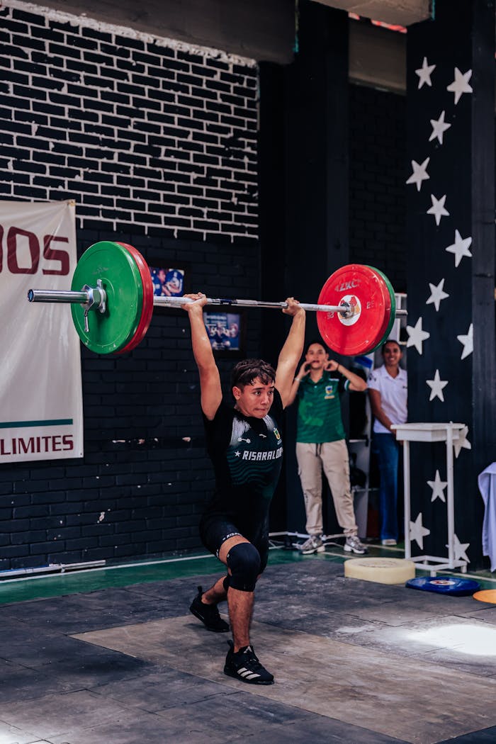 Young male athlete lifting weights in a dynamic indoor setting, showcasing strength and focus.